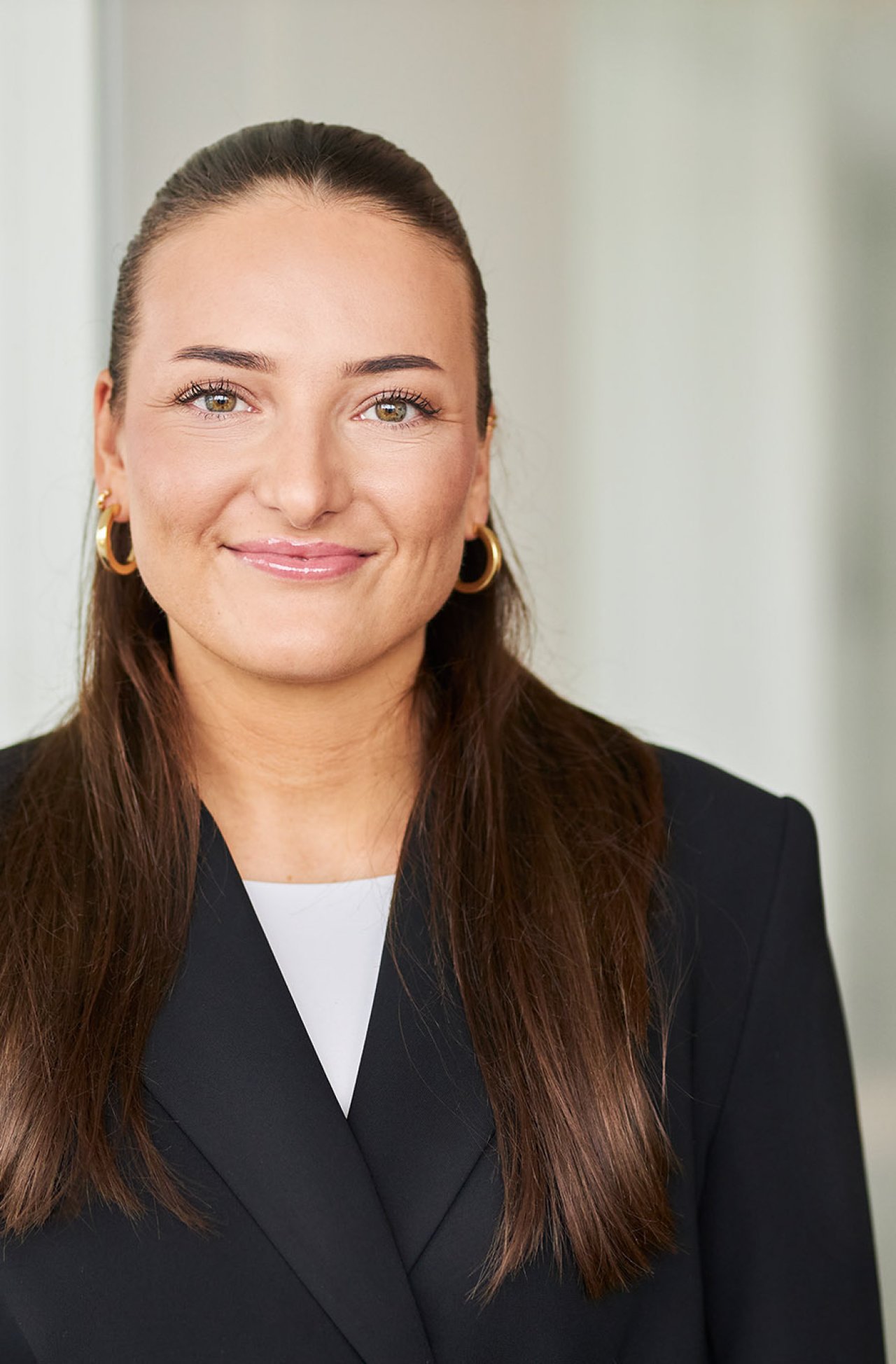 Eine junge Frau mit langen dunklen Haaren und Businessoutfit blickt in die Kamera.