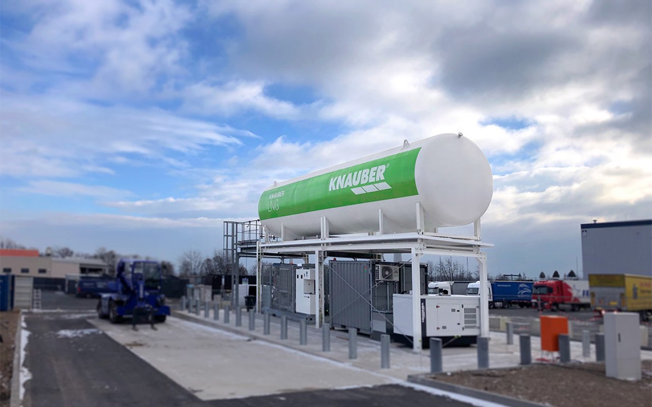 Große LNG-Tankanlage von Knauber mit aufgeständertem Flüssiggastank, Containern und Lkw im Hintergrund.