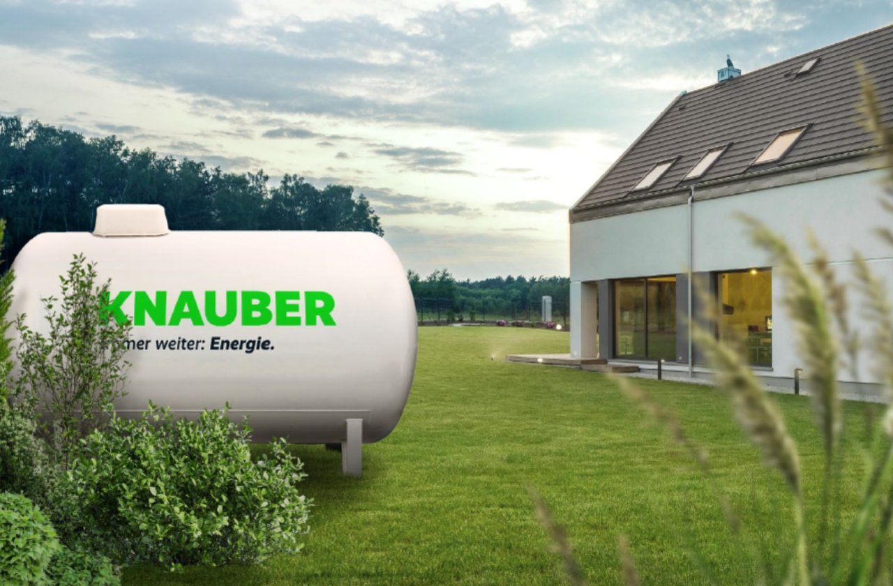 Ein Tank mit einem grünen Knauber Logo steht in einem Garten von einem Haus.
