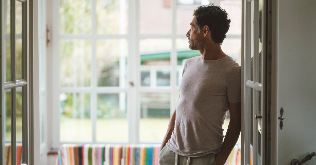Mann lehnt an Türrahmen und schaut in die Ferne.