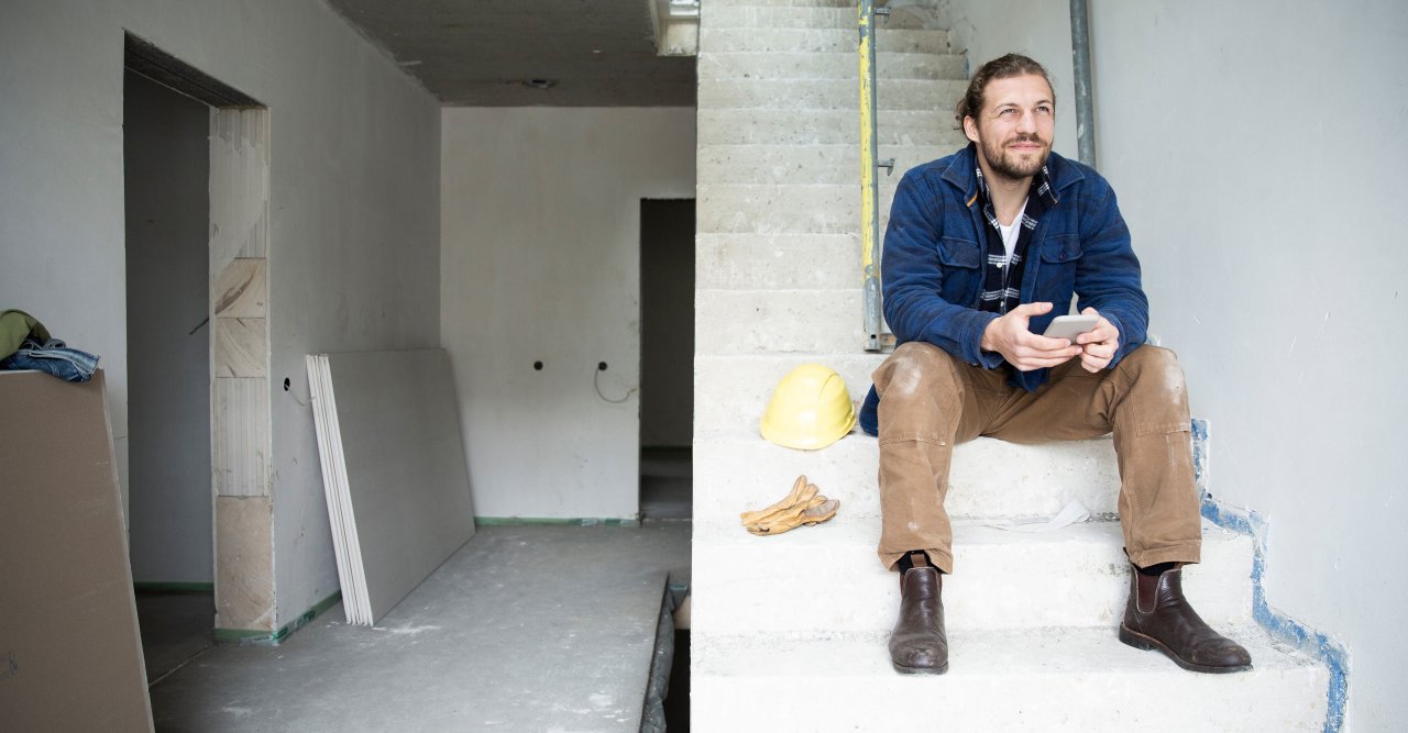 Ein junger Mann sitzt im Rohbau auf einer Kellertreppe.