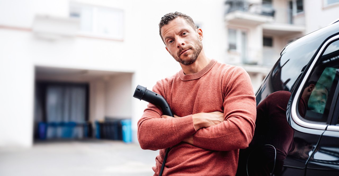 Ein Mann mit rotem Shirt mit einem Stromladekabel in der Hand.
