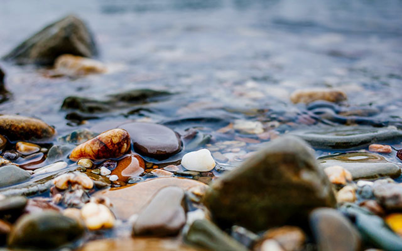 Nahaufnahme von bunten Steinen und Kiesel am Ufer mit Wasser, das sanft darüber fließt.