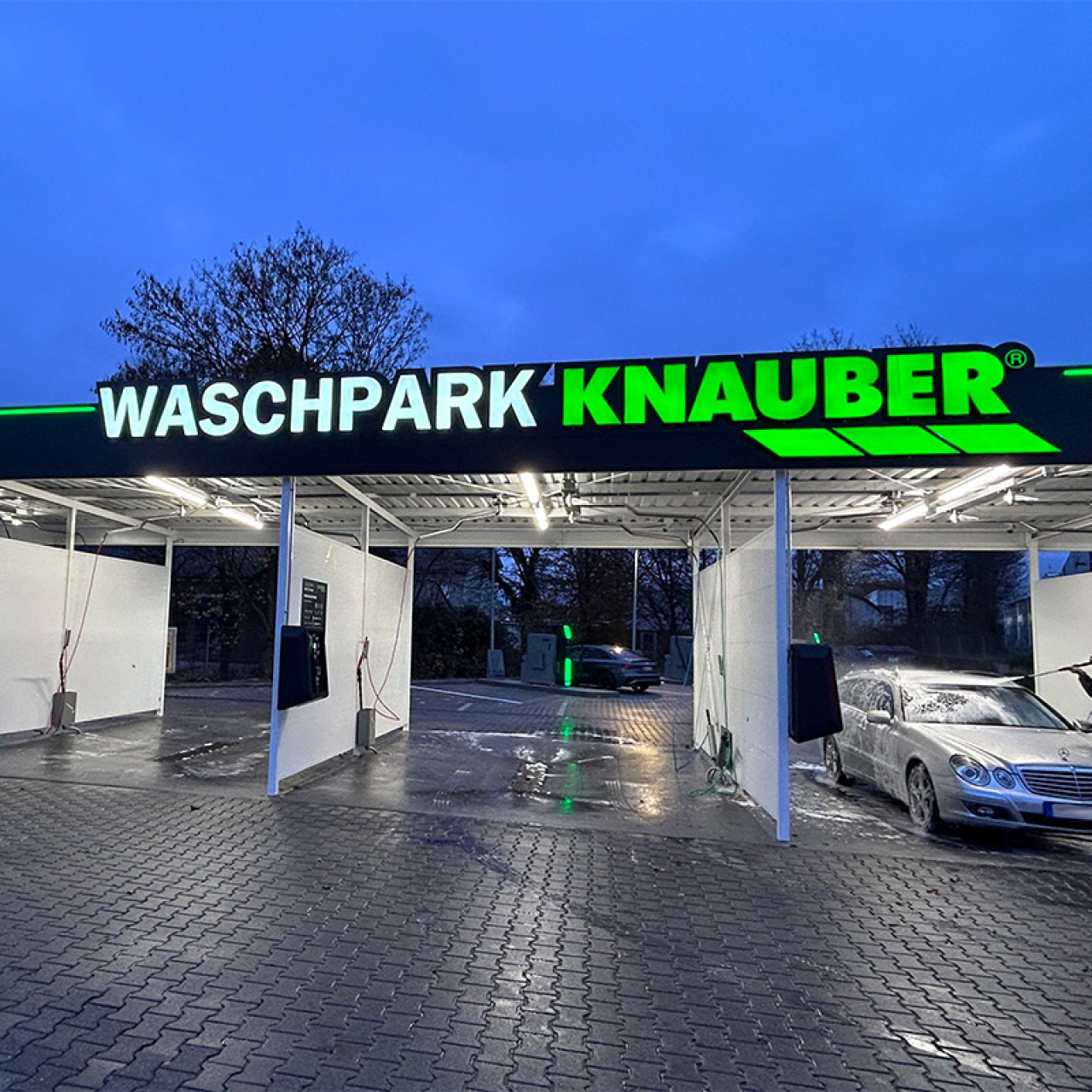 Auto wird abends im hell erleuchteten Knauber Waschpark mit Schaum eingesprüht, daneben freie Waschboxen.
